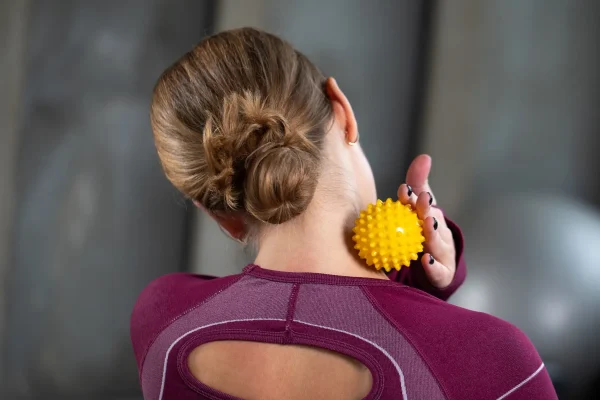 Sárga színű tüskés masszírozó labda alkalmazása nyakmasszázshoz